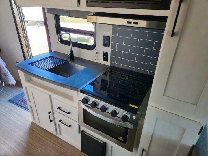 Modern RV rental kitchen with dark tile backsplash, stainless steel appliances, and a sink. Perfect for cooking on the road.. Palomino Puma 2022