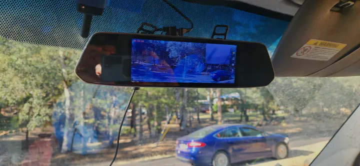View from inside a car, a dashcam rearview mirror displays a street scene with a blue car, possibly at an RV rental park.. Mercedes-Benz Sprinter 2011