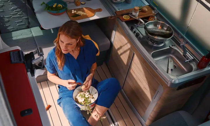 Woman prepares food in a modern RV rental kitchen. Cook fresh meals in your mobile camper van.. Volkswagen California T6.1 4MO 2024