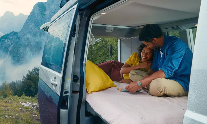 RV rental escape: A smiling couple enjoys a book inside their camper van, overlooking misty mountains.. Volkswagen California T6.1 4MO 2024