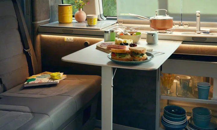 Interior of a modern rv rental, featuring a compact kitchenette & dining area with food, plus seating.. Volkswagen California T6.1 4MO 2024