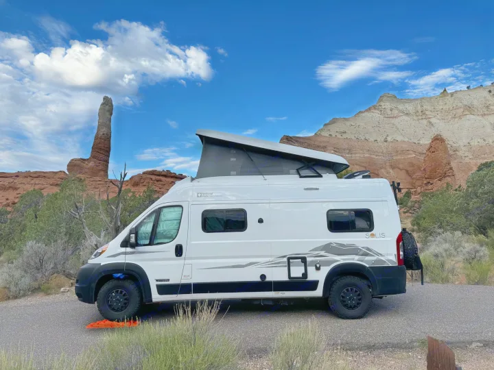 White Winnebago Solis RV rental with pop-top extended, parked by towering rock formations and layered mountains.. Winnebago Solis 2023