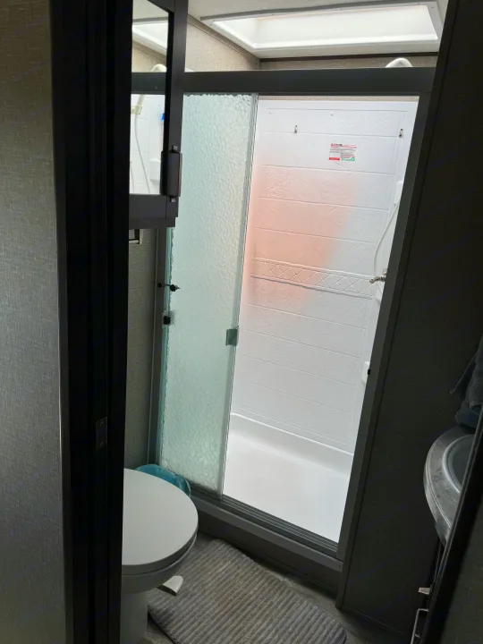 Step into this RV rental bathroom, featuring a modern shower stall, toilet, and sink area. Clean and compact.. Grand Design Reflection 2021