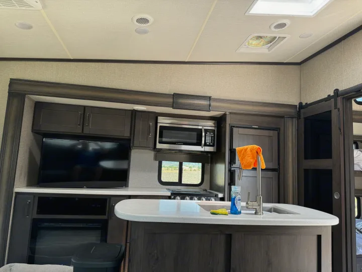 Modern **rv rental** interior: a functional kitchen island, TV, microwave, and full fridge. Great for travel.. Grand Design Reflection 2021