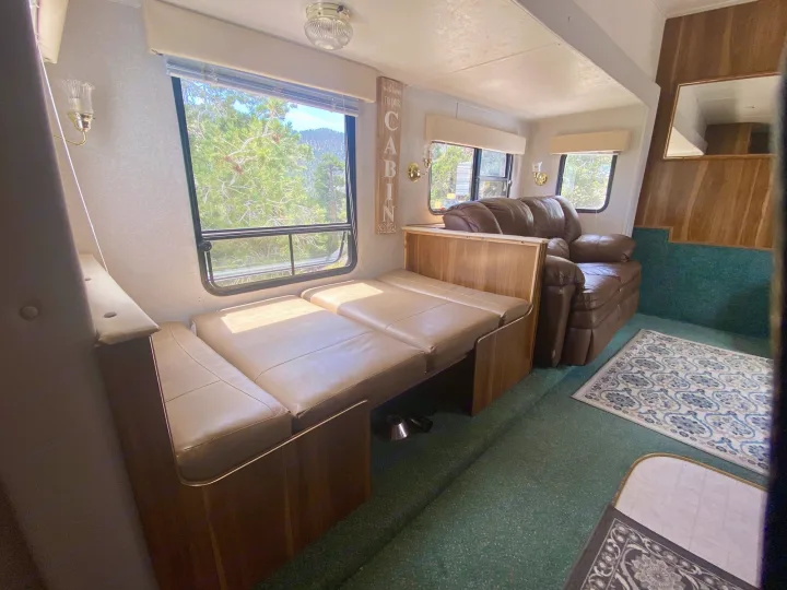 Cozy RV rental interior with a versatile dinette, scenic windows, and a comfortable leather sofa, offering nature views.. Forest River Cherokee Lite 2000