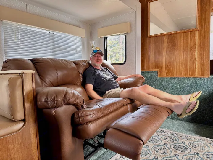 A happy man relaxes on an extended brown leather recliner inside an RV rental, showing the cozy and comfortable living space.. Forest River Cherokee Lite 2000