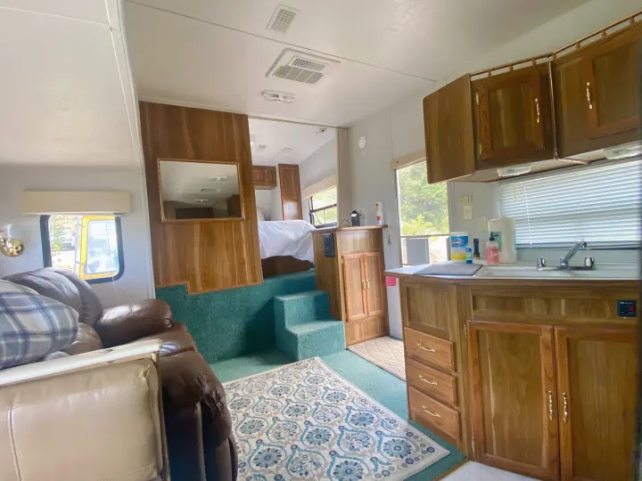 Inside a multi-level rv rental: living room, kitchen, and elevated bedroom with wood paneling and green carpet.. Forest River Cherokee Lite 2000