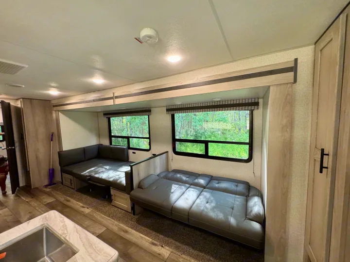 Spacious RV rental interior: two grey convertible sofas, large windows with greenery, and a cozy kitchen area.. Connect SE 2022