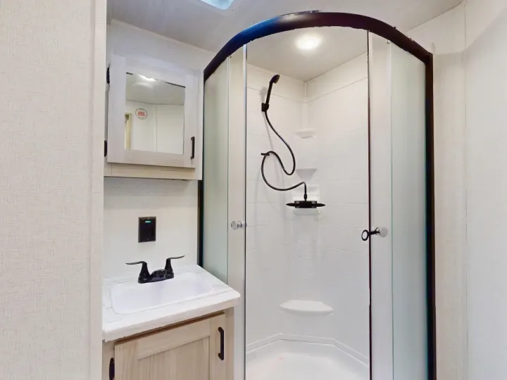 Clean RV rental bathroom features a compact shower, sink, and mirrored cabinet, ready for your trip.. East to West Silver Lake 3250QB 2025
