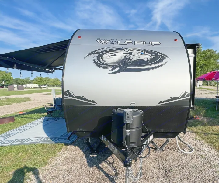 Front view of a silver Wolf Pup travel trailer at a sunny campsite, an ideal RV rental for outdoor adventures.. Forest River Cherokee Wolf Pup Black Label 2022