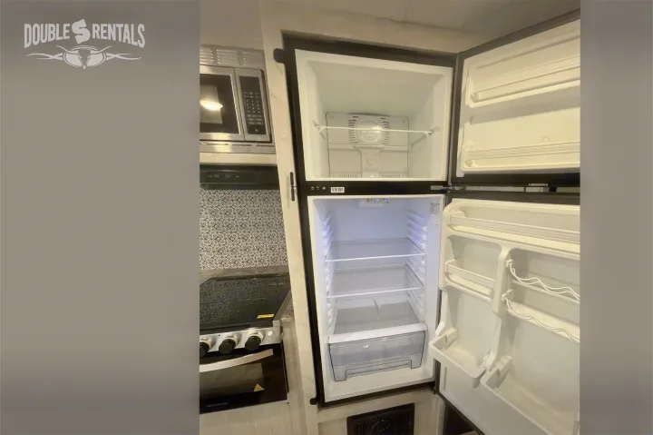 RV rental kitchen with open, empty refrigerator, freezer, microwave, and stove.. Shasta 26DB 2022