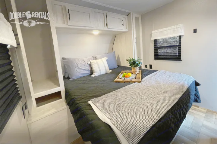 Comfortable RV rental bedroom with a plush bed, inviting linens, overhead storage, and a cozy window. Ideal for travel.. Shasta 26DB 2022