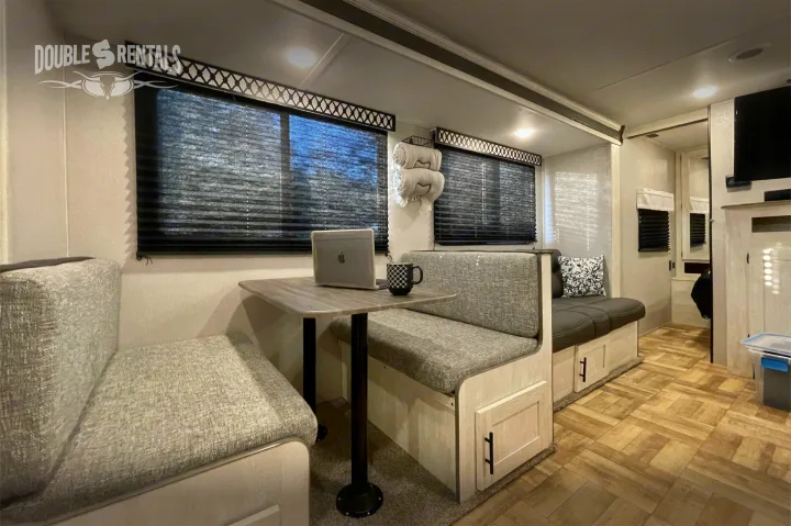 Cozy RV rental interior showcasing a modern dinette booth with a laptop and ample storage.. Shasta 26DB 2022