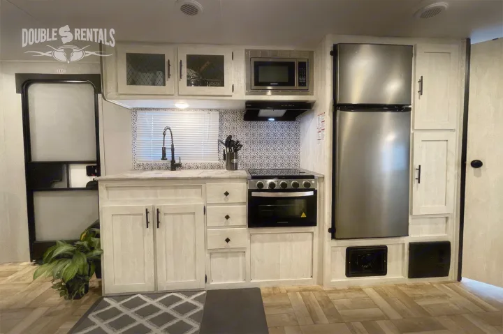 Modern RV rental kitchen showcasing stainless steel appliances, light cabinets, and a unique patterned backsplash.. Shasta 26DB 2022
