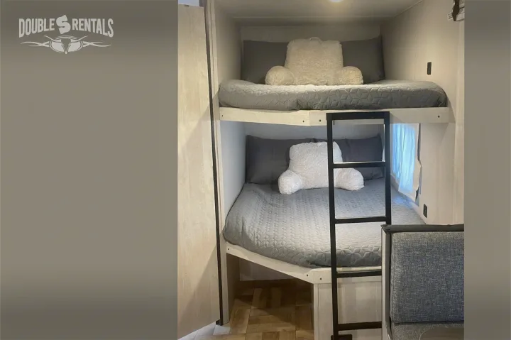 RV rental with cozy bunk beds. This travel trailer's sleeping area features two levels, grey bedding, and a ladder for comfort.. Shasta 26DB 2022