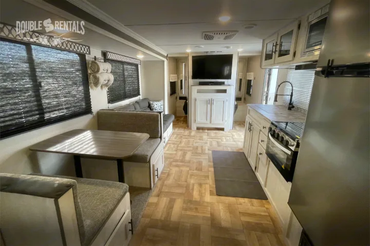 Bright RV rental interior featuring a dinette, sofa, full kitchen, and entertainment center, with light wood-look flooring.. Shasta 26DB 2022