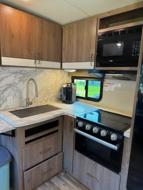 Well-appointed RV rental kitchen featuring a sink, microwave, oven, coffee maker, and stylish cabinetry.. Grand Design Imagine 2022