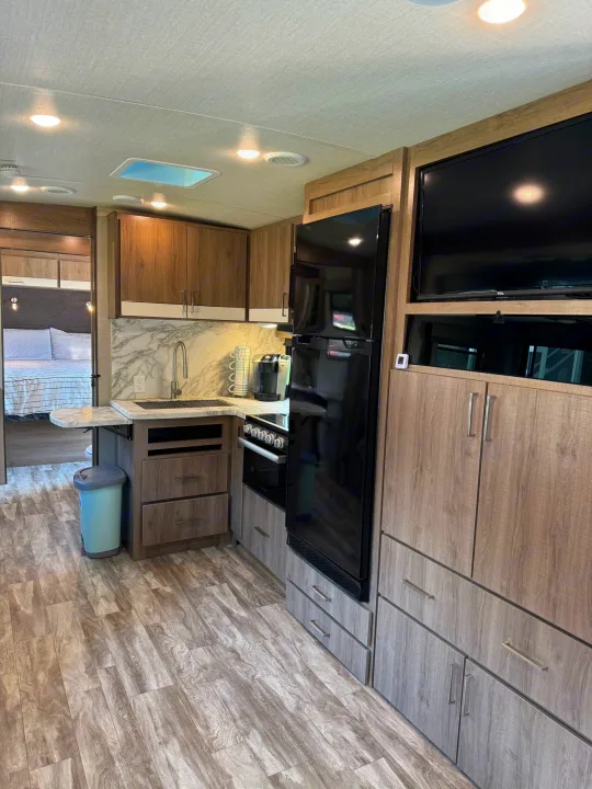 Modern RV rental interior: well-equipped kitchen with fridge, oven, sink, and a comfortable bedroom. Ideal for travel.. Grand Design Imagine 2022