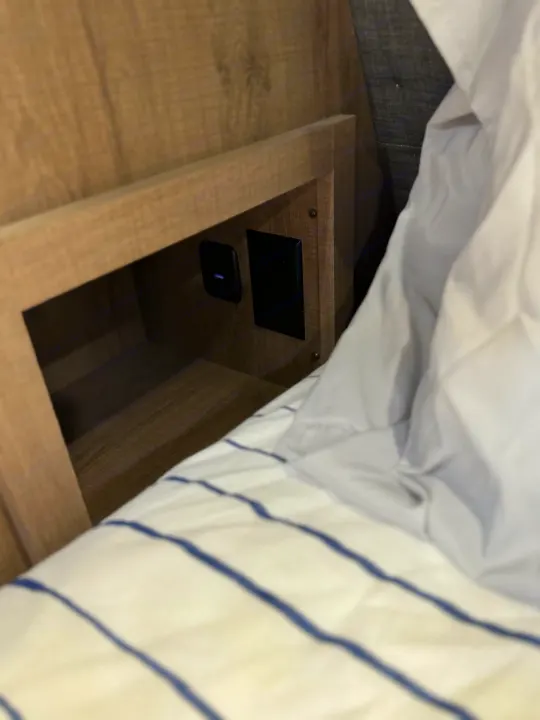 RV rental: Wooden built-in nightstand with power and USB outlets next to a bed with striped bedding.. Grand Design Imagine 2022
