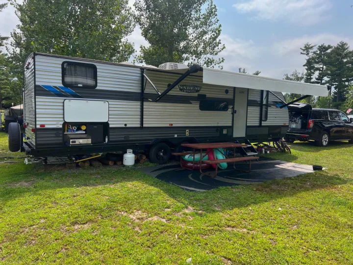 An RV rental is fully set up at a grassy campsite, featuring an awning, outdoor kitchen, and picnic area for outdoor living.. Forest River Salem Cruise Lite 2022