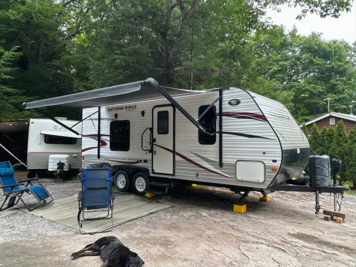 RV rental parked at a shaded campsite with an extended awning, outdoor chairs, and a dog relaxing.. Starcraft Autumn Ridge 2014