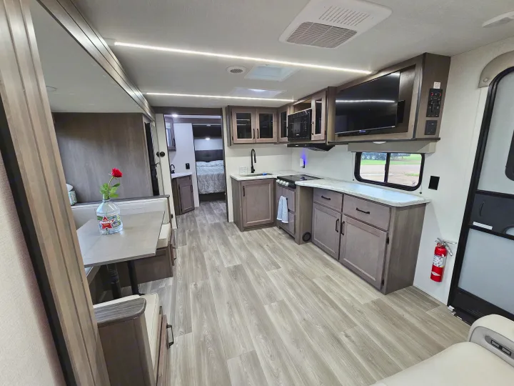 Modern RV rental interior showcasing a bright kitchen, comfortable dining booth, and peek into the bedroom. Light wood finishes.. Grand Design Transcend Xplor 2024