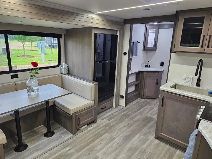 Spacious RV rental interior featuring a dinette, modern kitchen, and bathroom. A sign reads: "LOVE IS STAYING TOGETHER AFTER TRYING TO PARK THE CAMPER.". Grand Design Transcend Xplor 2024