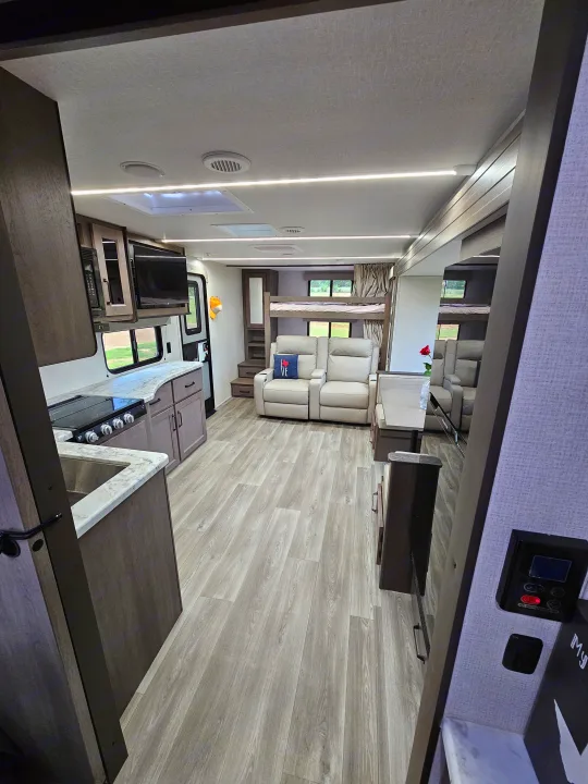 This RV rental interior features a modern kitchen, comfortable recliners, and bunk beds, all with bright, light wood-look flooring.. Grand Design Transcend Xplor 2024