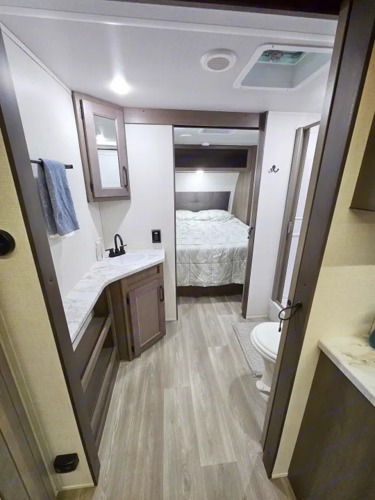 Modern RV rental interior with compact bathroom featuring a sink, mirror, and toilet, leading into a cozy bedroom.. Grand Design Transcend Xplor 2024
