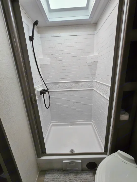 RV rental shower: Compact white stall with handheld showerhead, skylight, and textured walls, ready for use.. Grand Design Transcend Xplor 2024
