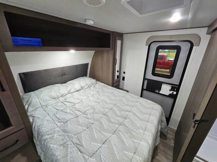 Cozy RV rental bedroom featuring a bed with patterned comforter, overhead cabinets, and an exterior door view.. Grand Design Transcend Xplor 2024
