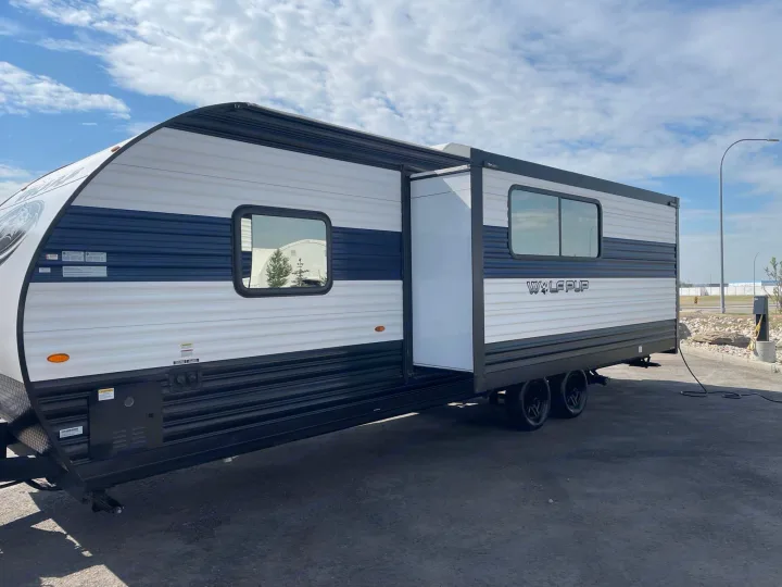 A white and blue Wolf Pup travel trailer RV rental is parked outdoors with its door open and power hookup.. Forest River Cherokee Wolf Pup 2023