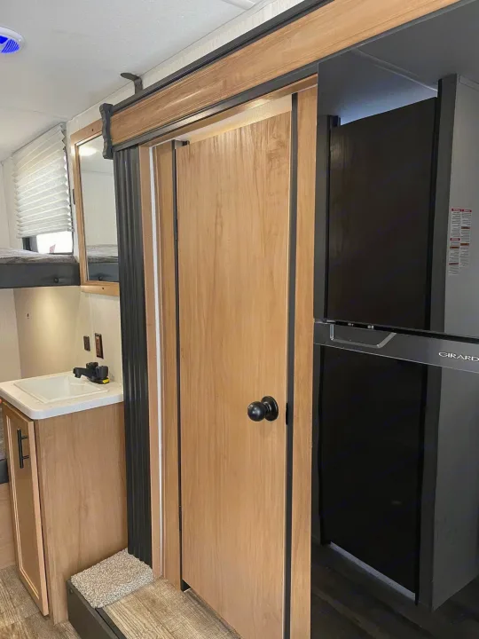 Compact RV rental interior featuring a sink, mirror, bunk bed, and a sliding door next to a refrigerator. Perfect for your next adventure!. Forest River Cherokee Wolf Pup 2023