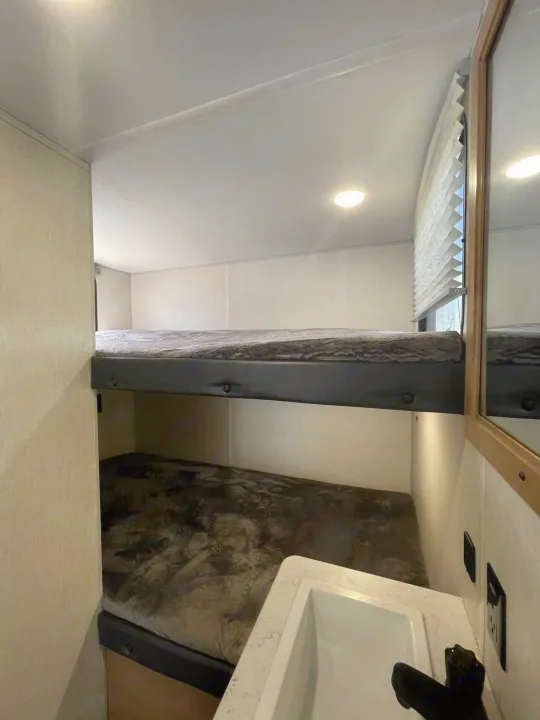 An RV rental interior features neatly made bunk beds and a small sink area, optimizing the compact space.. Forest River Cherokee Wolf Pup 2023