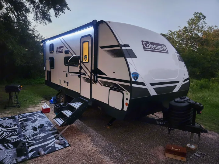 A modern Coleman RV parked at a serene campsite with evening lights on. Consider an RV rental for your next trip!. Dutchmen Coleman 1905BH 2024