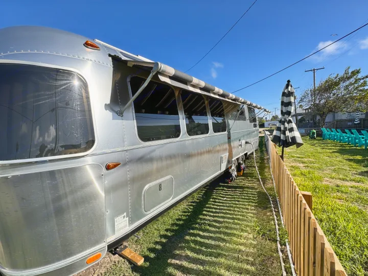 Experience an Airstream RV rental parked on vibrant green grass with its awning extended, perfect for a relaxing getaway.. Airstream Globetrotter 2020
