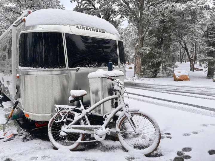 Snowy Airstream RV rental in a winter landscape, bike covered in snow. Perfect for cold-weather camping.. Airstream Globetrotter 2020