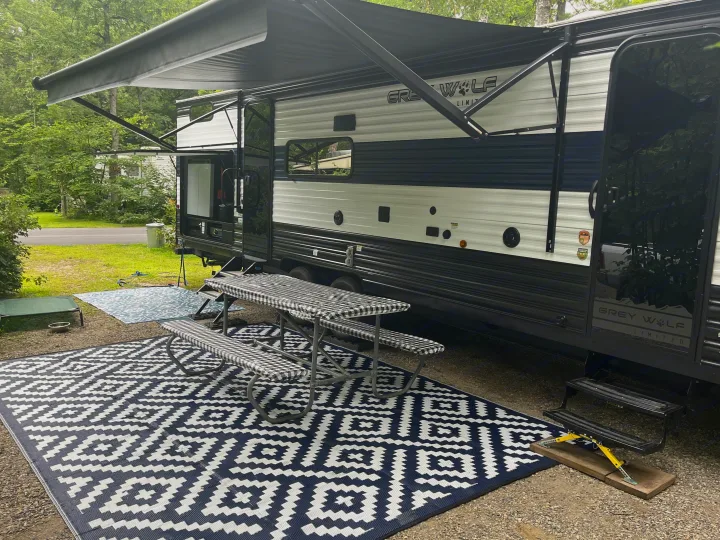 A Grey Wolf RV rental set up at a pleasant campsite with an awning, picnic table, and patterned outdoor rugs.. Forest River Grey Wolf 29TE 2024