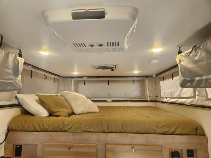Inside an RV rental: a comfortable bedroom with a made bed, AC, ceiling fan, and soft-sided sleeping area.. Palomino SS1500 2023