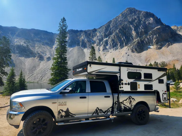 Silver Ram truck with a Palomino truck camper setup by a stunning mountain lake, ideal for an RV rental adventure.. Palomino SS1500 2023