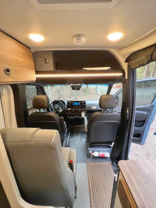 RV rental interior. Looking forward at the cockpit with comfy seats, dashboard, overhead LED lights, and storage cabinets.. Mercedes Sprinter Tiffin GH1 2024