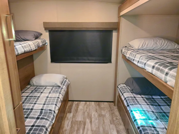 Cozy RV rental interior showing four bunk beds with plaid blankets and under-bed storage drawers.. Grand Design Imagine 2023