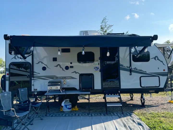 An RV rental equipped for outdoor living, featuring an extended awning, grill, and camping chairs.. Forest River Cherokee Wolf Pup Black Label 2022