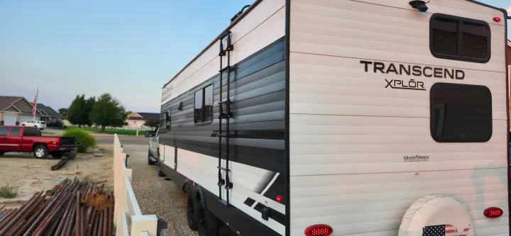 White and black Transcend XPLOR travel trailer, great for RV rental, parked on a residential street with ladder, windows, and a truck.. Grand Design Transcend Xplor 2022