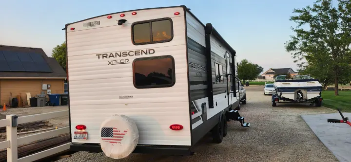 A Grand Design Transcend XPLÔR travel trailer, perfect for an RV rental, is parked on a gravel driveway next to a boat.. Grand Design Transcend Xplor 2022