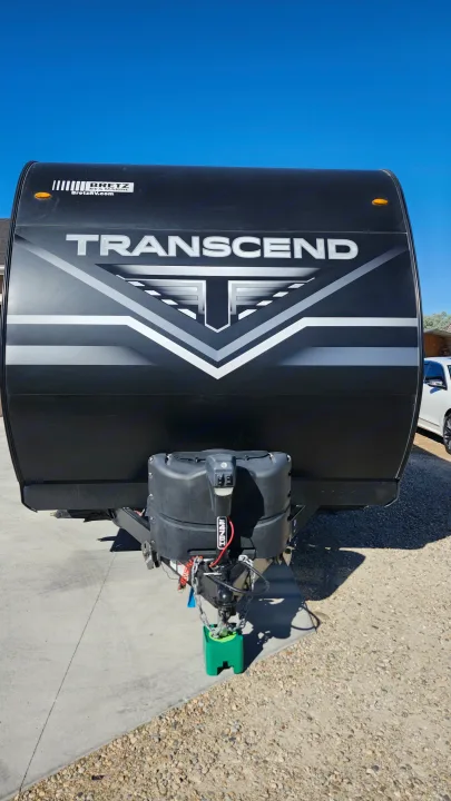 Black Transcend travel trailer for rv rental. Shows front, bold logo, propane tanks, and hitch system.. Grand Design Transcend Xplor 2022