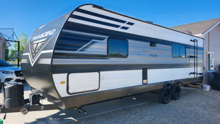 A sleek black, grey, and white Transcend Xplor travel trailer, perfect for RV rental, parked on a sunny residential driveway.. Grand Design Transcend Xplor 2022