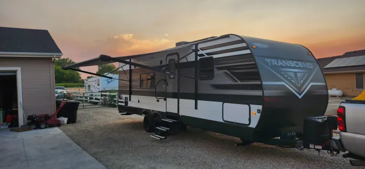 A modern Transcend travel trailer, great for an rv rental, with its awning extended on a gravel lot at sunset.. Grand Design Transcend Xplor 2022