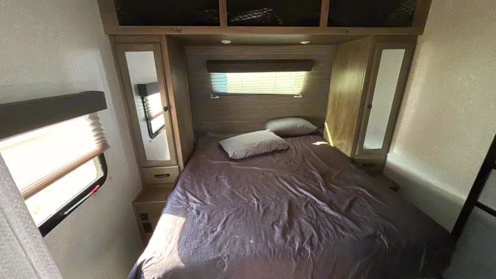 Cozy RV rental bedroom featuring a comfortable bed, integrated storage, and windows with blinds, ideal for travel.. Forest River Surveyor Legend 2023