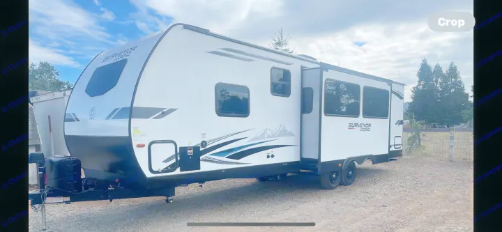 Ready for adventure? This white and black Surveyor Legend travel trailer makes an excellent RV rental option, parked outside.. Forest River Surveyor Legend 2023
